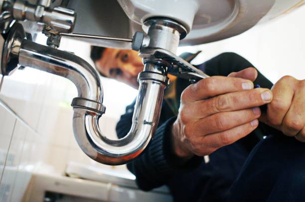 A plumber tightening a P-trap pipe underneath a sink with a wrench, focusing on the connection.