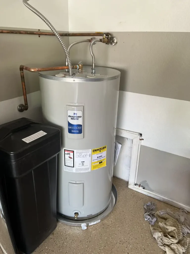 A tall, light gray Bradford White water heater stands in a utility area, next to a black bin and some discarded materials.