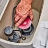 A close-up of a person's hand adjusting or repairing a Fluidmaster toilet flush valve and fill valve inside the tank of a white toilet, with beige tiled walls in the background.